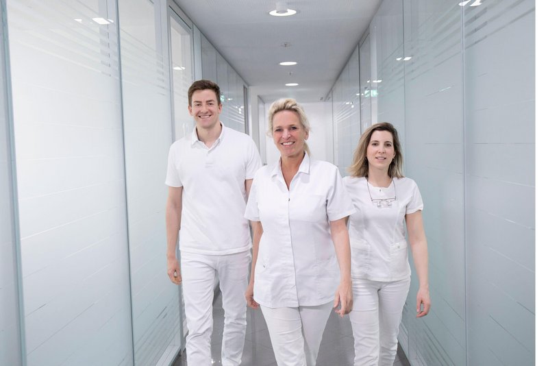 Drei Zahnärzte gehen durch den Gang der Klinik und lachen in die Kamera